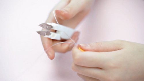 Hands trimming elastic cord close to the end of a yellow clay bead bracelet using small wire cutters