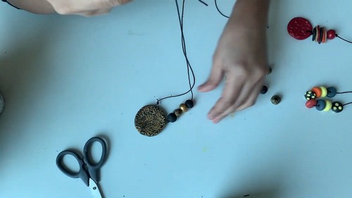 Finished clay necklaces with a textured gold pendant and colorful beaded strands arranged on a blue table.