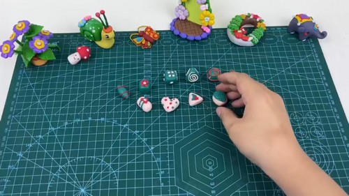 Assorted handmade clay beads with swirl, dot and heart patterns spread across a green cutting mat