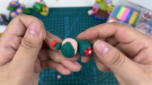 Threading a beading needle through a cream and green clay bead with red berry details