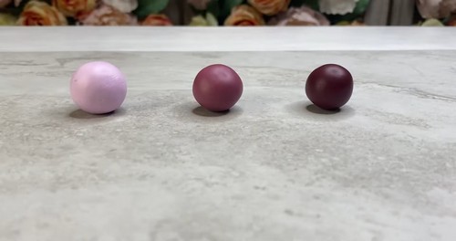Three smooth conditioned polymer clay balls in light pink, medium mauve, and dark burgundy lined up on a marble surface. 