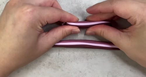 Hands bending and folding the layered pink and burgundy clay stack to begin building stripe repetition in the cane. 