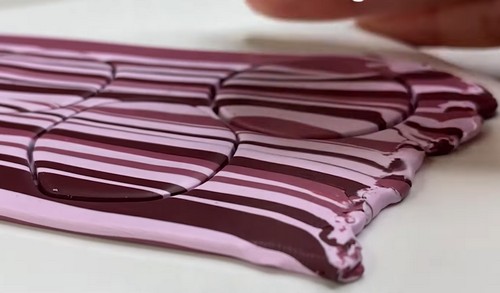 Close-up of a rolled-out polymer clay sheet showing a smooth diagonal stripe pattern in pink, mauve, and burgundy after being flattened and rolled. 