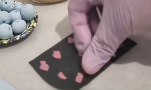 Placing small torn pieces of pink clay across the surface of a black clay sheet