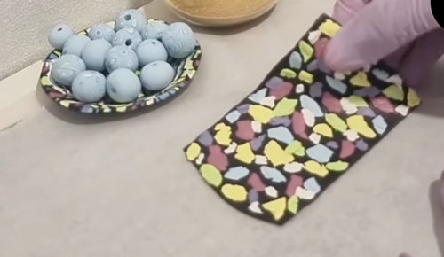 Black clay sheet covered in multicolored pastel clay pieces before being rolled and blended