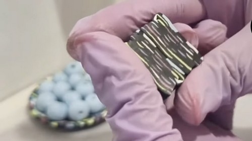 Gloved hands holding a folded clay block showing the marbled stripe pattern that forms after blending