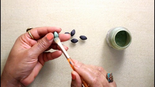 Six black clay balls lined up on a white ceramic tile before shaping.