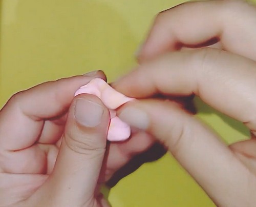Hands shaping a flat disc of light pink air-dry clay between the palms before ruffling.