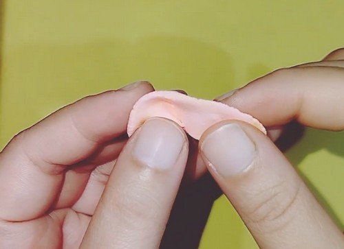 Fingertips pinching the edge of a clay disc to form raised ruffle folds around the perimeter.