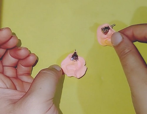 A matched pair of ruffled petal air-dry clay earrings drying face-up on a small foam pad.