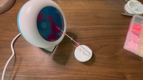 Elastic cord stretched from a bead spinner bowl to a small holder with pink clay beads threaded on