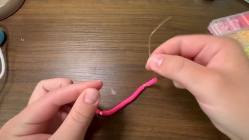 Hands sliding a short row of pink clay beads along the stretch cord