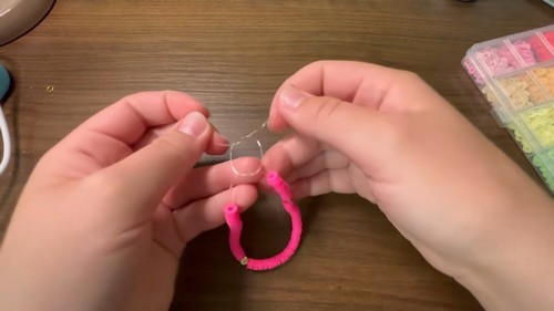 Checking the size of a pink clay bead bracelet by holding the loop of cord open
