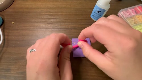 Tying off the elastic cord against a purple foam block to secure the bracelet