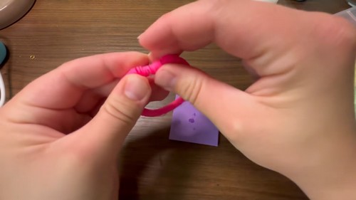 Working the knot back inside the row of pink clay beads to hide it