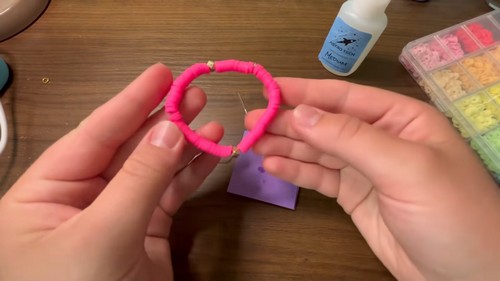 Completed pink clay bead bracelet held up with the needle and cord still nearby