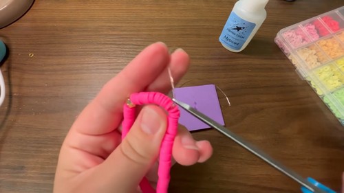 Cutting the excess cord tail close to the knot on a finished pink bracelet
