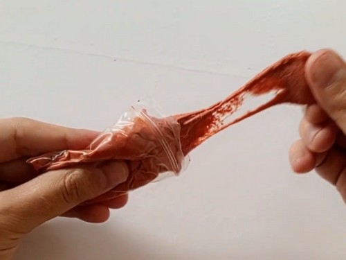 Hands pulling a bag of terracotta colored soft clay to show its stretchy texture before conditioning for bead making.