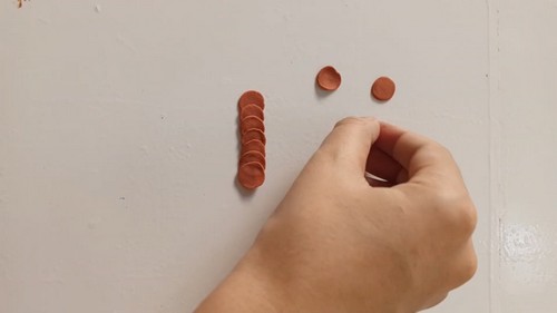 A hand arranging small flattened clay discs in a row on a white surface, with two rounded discs separated nearby ready to be rolled into rose shapes.