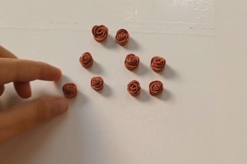 Eight completed terracotta clay rose beads arranged loosely on a white surface, with a hand placing one more into the group.