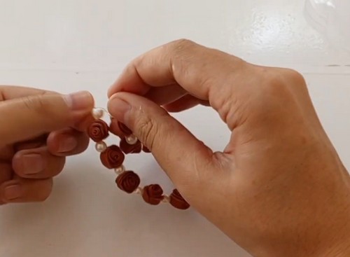 Hands stretching the nearly complete clay bead bracelet to check length, with rose beads and pearl beads alternating along the elastic.