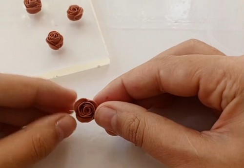 Hands holding a finished clay rose bead close up, showing the tight spiral petal detail built up from rolled clay discs.