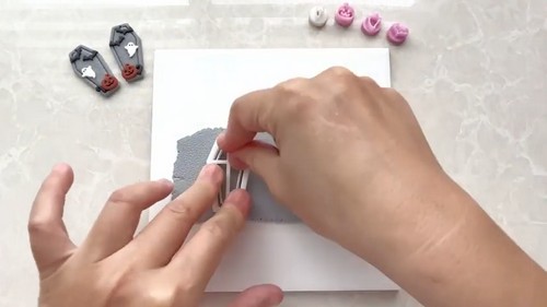 A textured grey polymer clay sheet with a coffin cutter pressed down to cut a Halloween earring base.
