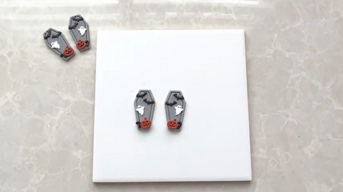 A finished pair of Halloween coffin polymer clay stud earrings displayed on a kraft earring card.
