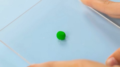 Small round green clay ball flattened between two fingers on a pale blue tile surface