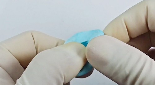 Gloved hands folding and pressing a small piece of teal polymer clay to begin conditioning it before building the cane.