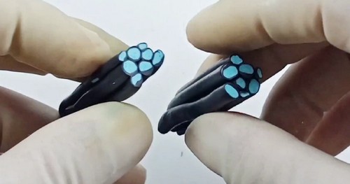 Gloved hands holding two black and teal polymer clay cane ends split open to reveal the circular teal dot pattern inside the black outer layer.