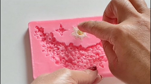 Metal spatula cleaning excess clay from the edge of a filled flower mold.
