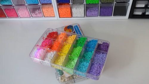 Clear storage cases filled with heishi clay beads sorted by color, with more bead trays on the shelf behind