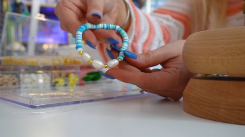 Finished blue and turquoise clay bead bracelet with freshwater pearls and gold beads held up in one hand