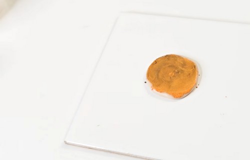 Flattened clay circle on a tile with orange and gold mica powder blended across the surface