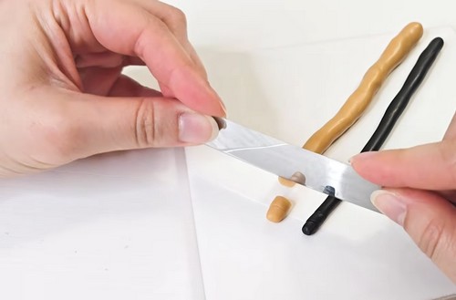 Blade slicing small segments from gold and black clay logs on a white surface