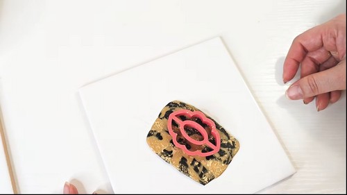 Pink oval cutter pressed into a sheet of black and gold marbled clay on a white tile
