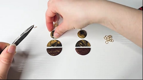 Pliers and jump rings laid beside two assembled tortoise shell clay earring sets being linked together on a white surface