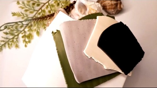 Four sheets of polymer clay in olive, grey, off-white and speckled black cut into a diamond grid with a blade.