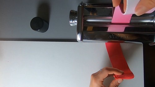 A thin strip of pink polymer clay being rolled into a rose bud centre by hand.