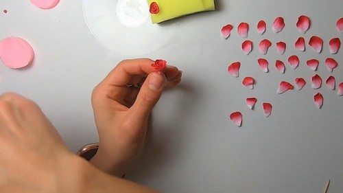 A fingertip curling the thin top edge of a pale pink clay petal outward.